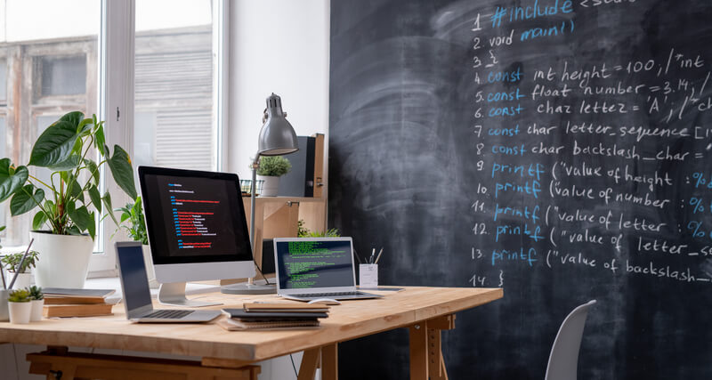 Schreibtisch mit Laptop und einer Tafel mit IT Themen
